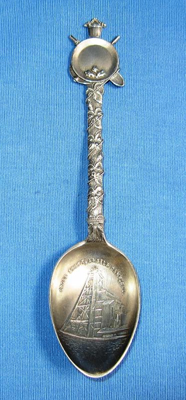 Souvenir Mining Spoon Cross Shaft.JPG - SOUVENIR MINING SPOON CROSS SHAFT UTICA MINE - Sterling silver spoon, 5 1/8 in. long, embossed mining scene in bowl with engraved CROSS SHAFT, ANGELS CAMP, CAL. in bowl, ca. 1900, back with sterling marking, handle has gold pan with crossed pick and shovel at top and a silver rope extending from a bucket ontop and wrapped around handle shaft  [The Utica Mine, one on the best-known gold mines in the Mother Lode, is located within the city of Angels Camp in southwestern Calaveras County, California. The gold mines in and around Angels Camp are part of the Angels Camp mining district, which is credited with producing at least $30 million in gold. The Utica Mine alone is thought to have produced in excess of $17 million at the old price of gold and during the 1890s, the Utica Mine was one of the most productive in the nation. The surface of the Utica claim was mined during the early part of the gold rush, but large-scale development was only conducted between 1893 and 1915 by the Utica Gold Mining Company.  In the 1880s Charles D. Lane gained control of the Utica claim and along with partners Walter Hobart and Alvinza Hayward, organized the Utica Mining Company and started large scale development in 1893. The other claims that now constitute the Utica Mine (Brown, Confidence, Dead Horse, Jackson, Little Nugget, Raspberry, Stickle, and Washington claims) were gradually acquired and the mine was developed on a major scale with more than 500 men on the payroll.  In 1896, the Cross shaft was sunk in hard rock to provide a permanent opening for the mine.  By 1900, the Cross vertical shaft bottomed at 1312 feet.  Details of mine workings are sketchy, but there are thought to be over 100 miles of underground workings.  Operations continued into late 1915 when the mine was shut down.  Except for mill cleanups and small amounts of gold recovered from the dump in the 1930s, the mine has been idle since.]